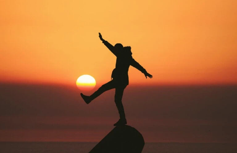 A man balancing on a rock at sunset